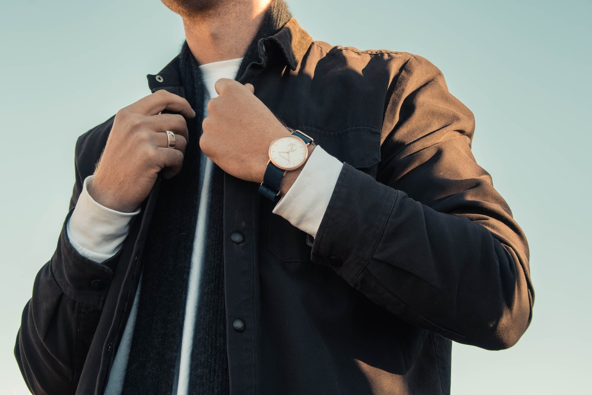 Schlichte Armbanduhr mit weißem Zifferblatt und roségoldenem Gehäuse an einem dunklen Textilband