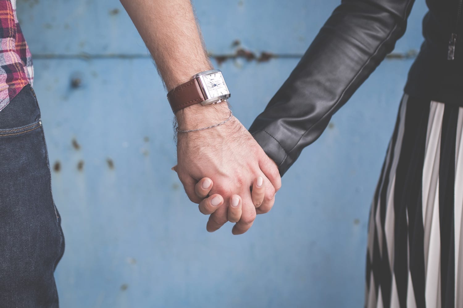 Männerhand mit eckiger Armbanduhr an braunem Lederarmband, Hand in Hand mit einer Frau
