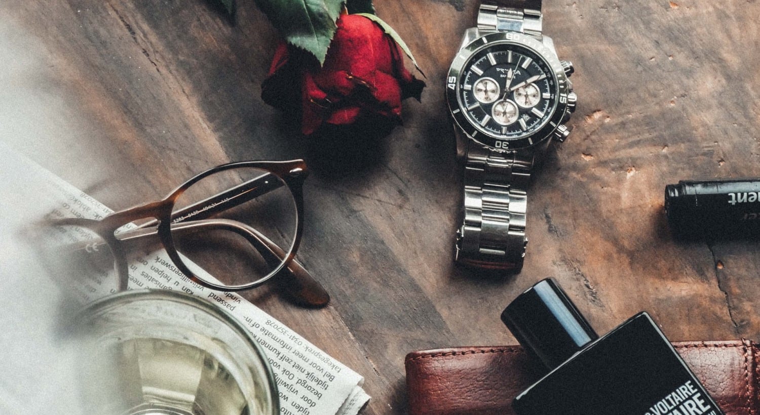 Chronograph, Lesebrille und Zeitung auf einer Holzplatte